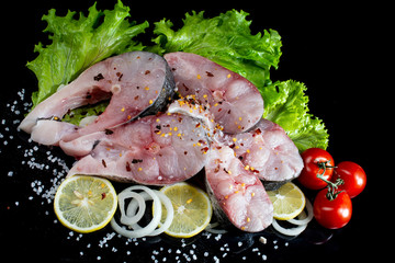 fish steaks with lettuce spices and tomatoes on a black background