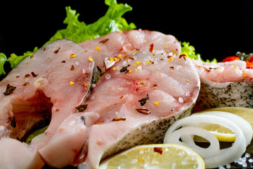 fish steaks with lettuce spices and tomatoes on a black background