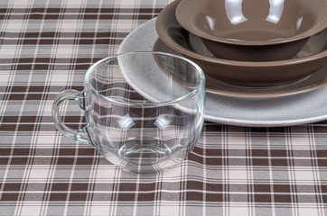 Empty glass mug and a set of ceramic plates on a table covered with a checkered tablecloth, close-up