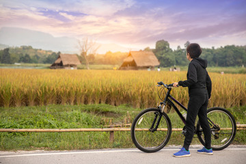 Fototapeta premium Woman standing with bike looking at rice field , Bike at the summer sunset in the nature. Bicycle and ecology lifestyle concept.