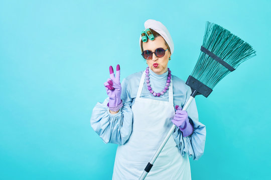 Cleaning Lady Fun. Elderly funny housewife fooling around with a broom. Full body isolated blue. Comical cleaning lady, old woman funky