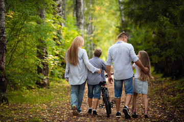 Fototapeta premium Rear view - a family with two children walks in park