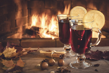 Two glasses of mulled wine on a wooden table in front of a burning fireplace