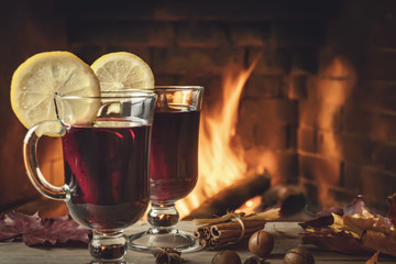 Two glasses of mulled wine on a wooden table in front of a burning fireplace