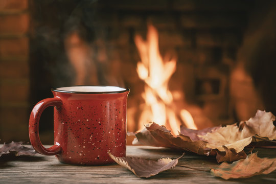 Red mug with hot tea in front of a burning fireplace, comfort and warmth of the hearth concept