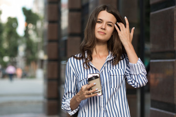 Businesswoman uses a mobile phone, walking along the city streets with coffee in her hand.