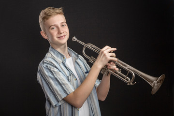 The young Boy plays jazz on a trumpet in front of dark background