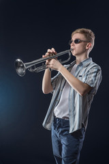 The young Boy plays jazz on a trumpet in front of dark background