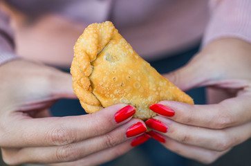 Young woman eating traditional fried Spanish and Argentine empanadas at a street food market