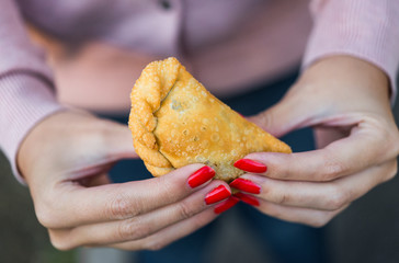 Young woman eating traditional fried Spanish and Argentine empanadas at a street food market