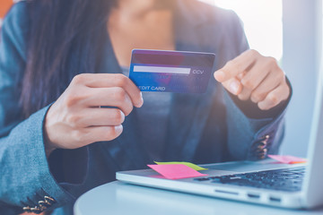 Business women are carrying credit cards and using laptop computers to order products online.