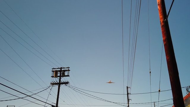 Plane flies overhead in blue sky. Tilt up shot through power lines.