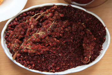 Dried sumac seasoning in a wooden bowl, top view. a handful of red sumac powder in a plate abstract background . Sumak grains and powder . Sumac is in a white plate .
