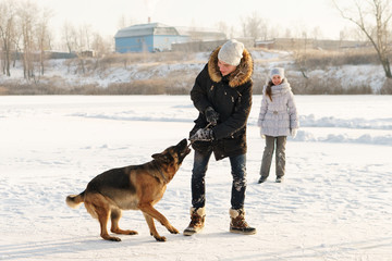 Joyful teens spend time together with lovely pet German Shepherd Dog on a walk in the winter park on a sunny day. Having fun playing in snow outdoors. Time for cheery. Happy family. Playful mood