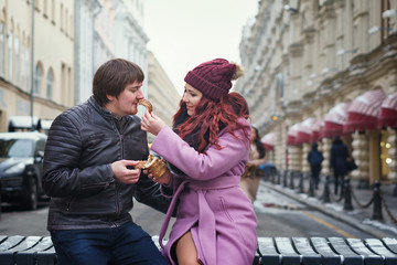Fototapeta premium Portrait of beautiful young couple eating Trdelník in the street. Having fun in winter of the european city. Vacation and holiday concept