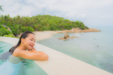 Portrait young asian woman relax smile happy around outdoor swimming pool in hotel resort with sea ocean view