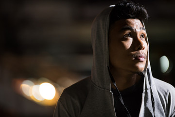 Face of young Asian man with hoodie thinking in the city streets at night