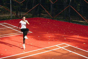 Fototapeta premium Sport woman jumping and stretching. Young female doing morning exercises in a sport park.