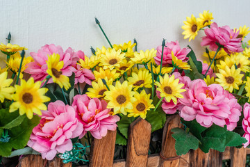 Bed of pink yellow artificial plastic flowers guarded by wooden fence