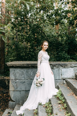 Plakat Wedding in the European style in nature. A bride in a white dress on a stone staircase.