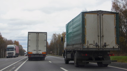 Trucks overtaking, vehicles moving on autumn asphalt highway, road rules, traffic, lorry rear view