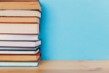 A simple composition of many hardback books, raw books on a wooden table and a bright blue background