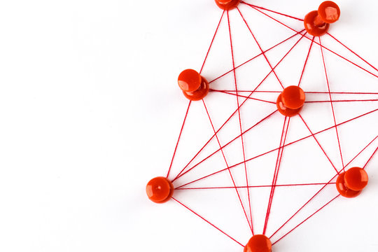 Network With Red Pins And String,  Linked Together With String On A White Background Suggesting A Network Of Connections.