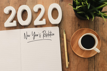 Business concept of top view 2020 year's resolution list with notebook, cup of coffee over wooden...