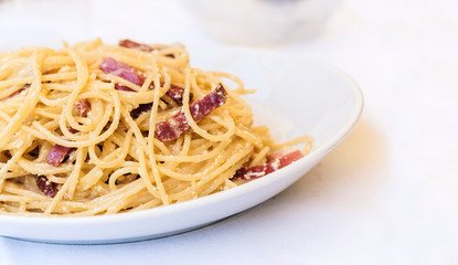 Pasta carbonara spaghetti with ham, bacon and fresh parmesan on the white plate in restaurant in Catania, Sicily, Italy.