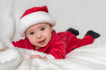 Little baby in Santa Claus costume is lying on white blanket