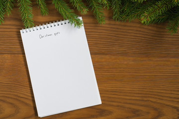 Flat lay christmas gift list notepad with spruce twigs on ash wood surface