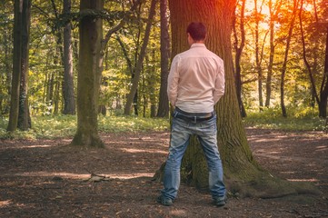 Standing man peeing near big tree in autumn forest