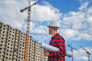 civil engineer in a white helmet and plaid shirt on the background of a house under construction