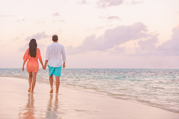 Luxury romantic Caribbean getaway for lovers walking on sunset beach stroll for honeymoon destination. Woman and man couple holding hands going away.
