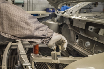 The hands of a mechanic in white protective gloves install a screw bump in the engine compartment of the car body