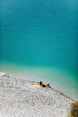 Fototapeta na wymiar woman sitting at sand beach looking at blue azure water