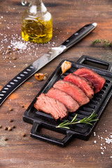 Grilled sliced beef steak with salt, garlic and rosemary on stone cutting board.