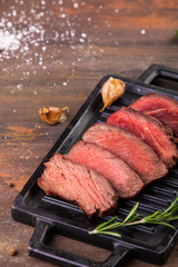 Grilled sliced beef steak with salt, garlic and rosemary on stone cutting board.