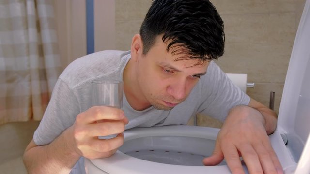 Portrait of man is vomiting in toilet and drinking water feeling bad having flu. Food poisoning and vomiting, cold and flu with high temperature. Sickness man at home with nausea.