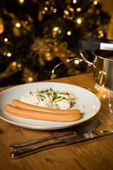 Wiener Würstchen und Kartoffelsalat als typisches Weihnachtsessen zu Heiligabend in Deutschland am Weihnachtsbaum mit Weihnachtsdekoration und Lichterketten