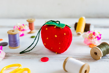 Handmade and needlework. Pin cushion strawberry with a simple ornament and a pair of scissors on a white table. Sewing supplies in the background. Close up