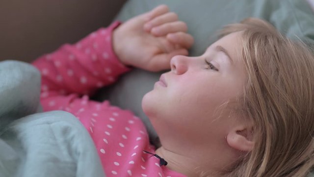 Portrait of a small girl sick with fever and a woman's hand touching her. Mother caring for sick child lying in bed with flu
