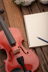 Obraz na płótnie Canvas Close-up shot violin orchestra instrumental and notebook over wooden background select focus shallow depth of field