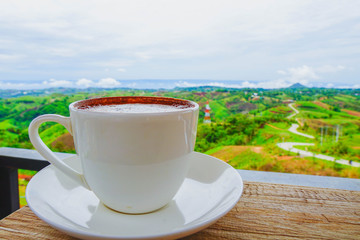 White hot coffee mugs placed on a wooden floor with green fresh mountain and morning fog as background