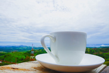 White hot coffee mugs placed on a wooden floor with green fresh mountain and morning fog as background