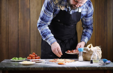 man preparing a pizza, knead the dough and puts ingredients