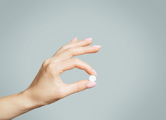 Female hand holding a round white pill or vitamin. - 300292763