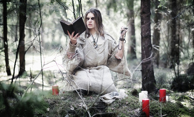 Fototapeta na wymiar Fairy magician. A sorcerer with a glass sphere, a magical spell and a ritual. Elder with a staff and a cross in the forest. Black and white magic. A spell in an old book.