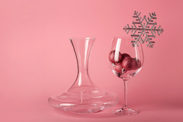 The wine glass with Christmas balls inside, decorated with silver snowflake on the pink background. The mockup for Christmas and  New Year. Wine decanter.