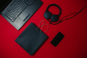 Black friday image with space for text. Bkack friday sale flat lay. Black friday bag, notebook, headphones and mobile phone on the red background.